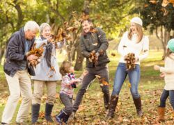 Auf dem Bild sind Großeltern, Eltern und zwei Kinder zu sehen, die bei gutem Herbstwetter mit Blättern spielen