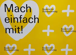 gelbe Wand mit weißen Herzen und Aufschrift "Mach einfach mit! Bayerischer Präventionstag"