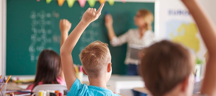 Zwei Schüler und eine Schülerin melden sich in der Klasse, die Lehrerin steht an der Tafel