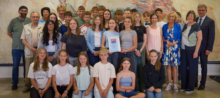 Schulklasse mit Mitgliedern des Elternbeirats und Vertretern aus Schule und Politik. In der Mitte wird die Urkunde für den bayerischen Hauptpreis gehalten.