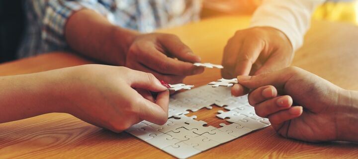 Unser Angebot vier Hände die jeweils ein Puzzleteil halten und zu einem Gesamtpuzzle einfügen