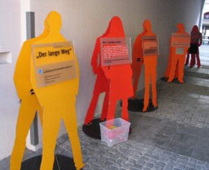 Der lange Weg Fünf Figuren der Ausstellung "Der lange Weg" sind an einer Mauer zu sehen.